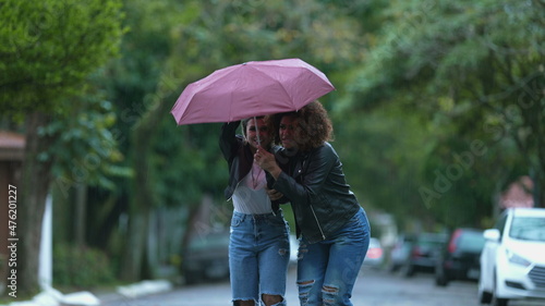 Friends sharing umbrella together during rainy day © Marco