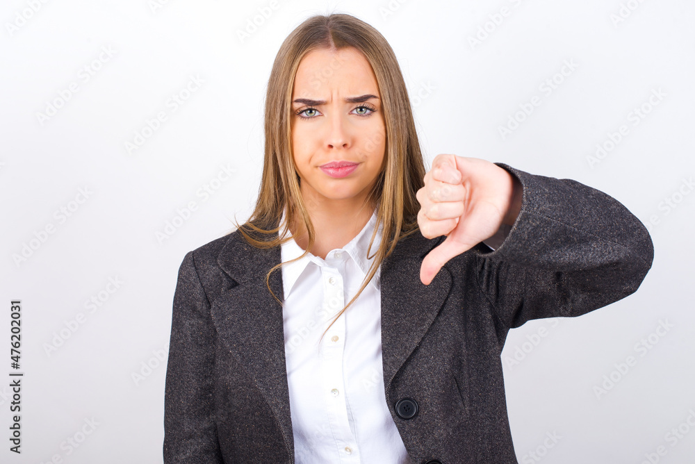 Young business woman wearing jacket over white background looking unhappy and angry showing rejection and negative with thumbs down gesture. Bad expression. Young business woman wearing jacket over white background looking unhappy and angry showing rejection and negative with thumbs down gesture. Bad expression.