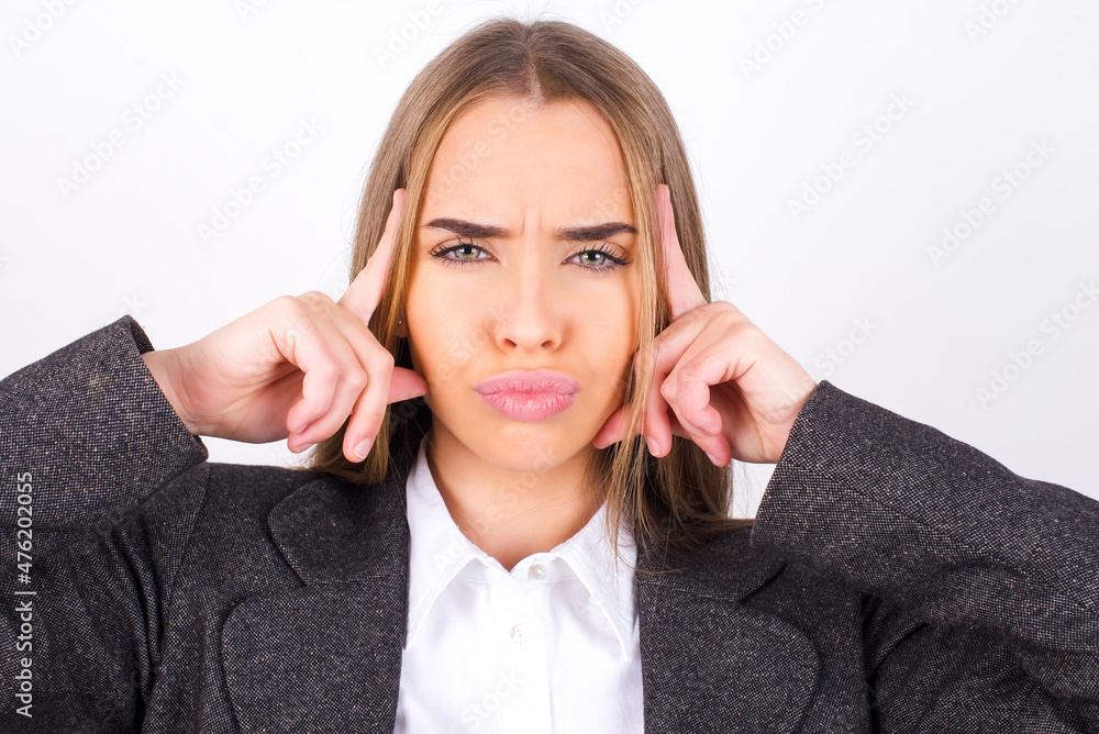 Serious concentrated Young business woman wearing jacket over white background keeps fingers on temples, tries to ease tension, gather with thoughts and remember important information for exam Serious concentrated Young business woman wearing jacket over white background keeps fingers on temples, tries to ease tension, gather with thoughts and remember important information for exam