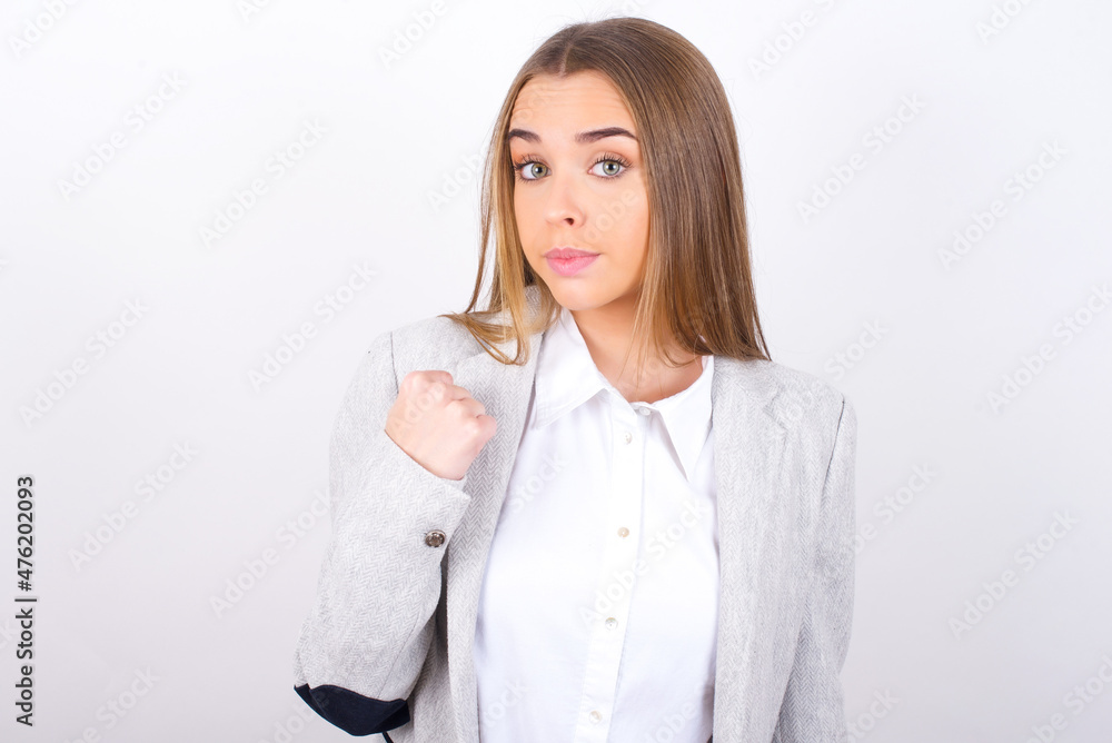 Young business woman wearing jacket over white background shows fist has annoyed face expression going to revenge or threaten someone makes serious look. I will show you who is boss Young business woman wearing jacket over white background shows fist has annoyed face expression going to revenge or threaten someone makes serious look. I will show you who is boss