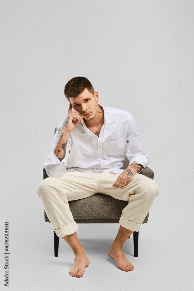 Full length portrait of young barefoot man in shirt and jeans sitting sitting in armchair Full length portrait of young barefoot man in shirt and jeans sitting sitting in armchair