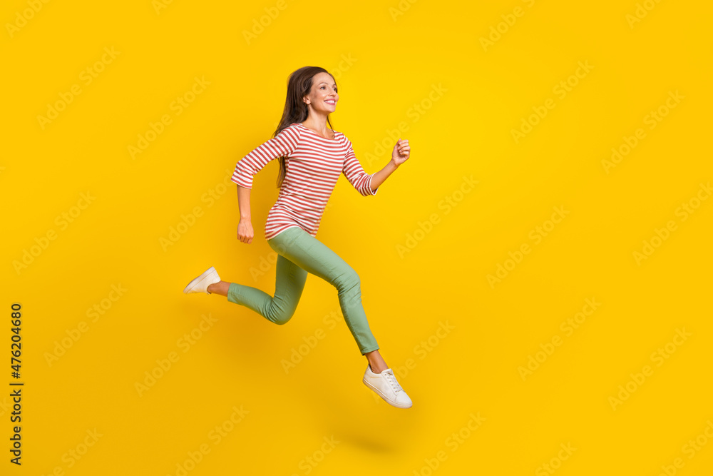 Photo of sweet charming mature lady dressed striped shirt running fast jumping high empty space smiling isolated yellow color background