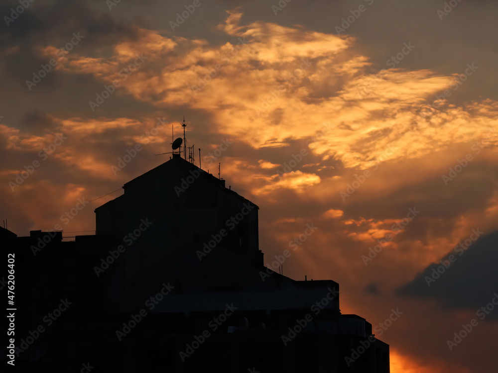 Silhouette of building with antennas on the top and cloudy sky at sunset