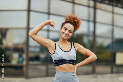 A young, strong, and happy sportswoman is showing her biceps while standing outdoors. Strength comes with effort and persistence, and the benefits are a happier and healthier life.