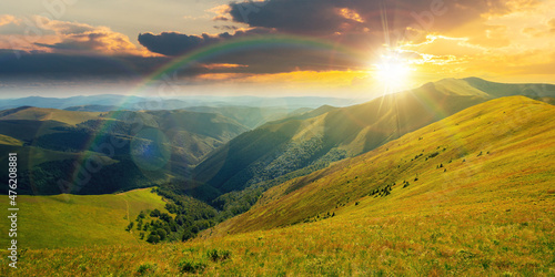 mountain landscape in summer at sunset. grassy meadows on the hills rolling in to the distant peak beneath a rainbow in evening light photo