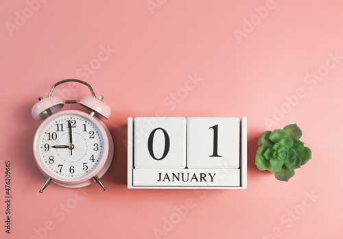 wooden calendar 01 January, pink vintage alarm clock 9 o'clock and succulent plant pot on pink background. First morning of new year. photo