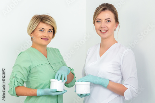 Two cosmeticians with jars of wax for depilation smiling against a white background. Natural product for hair removal. Copy space