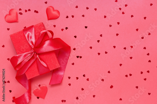 Red gift box tied with a ribbon with decorative hearts on a red background. Gift for Valentine s.