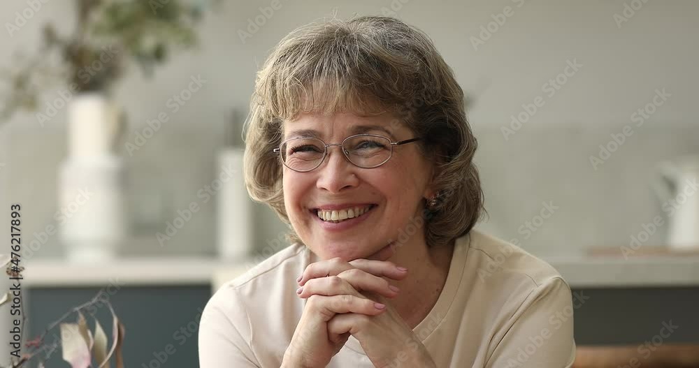 Pleasant middle age woman in eyeglasses housewife teacher retiree posing for portrait at cozy home. Positive pretty single older adult female look at camera with healthy beautiful smile enjoying life Pleasant middle age woman in eyeglasses housewife teacher retiree posing for portrait at cozy home. Positive pretty single older adult female look at camera with healthy beautiful smile enjoying life