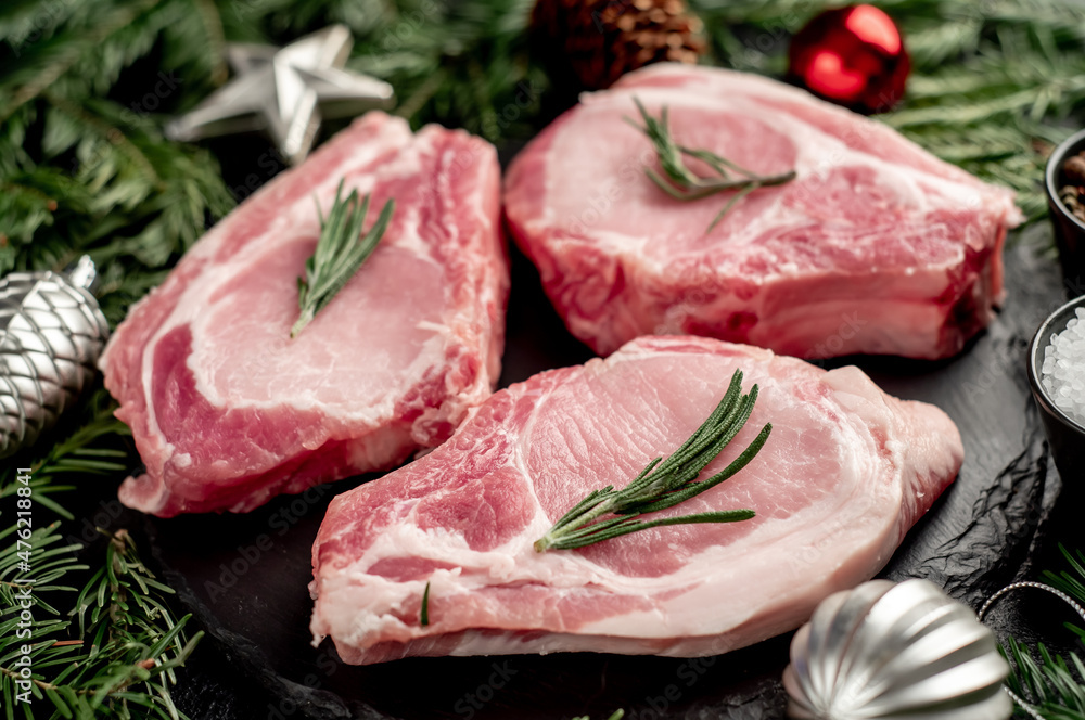 Christmas raw pork steaks, with fir tree and new year decorations on stone background