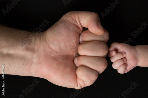 Newborn's fist in front of dad's fist on black background