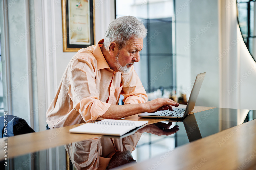 A smart senior student is sitting at home and typing homework on his laptop. Retraining concept. A smart senior student is sitting at home and typing homework on his laptop. Retraining concept.