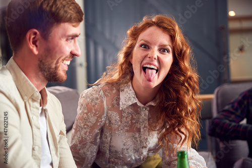 Woman In Young Couple Making Face Sitting On Sofa Talking Together As Friends Meet At Home