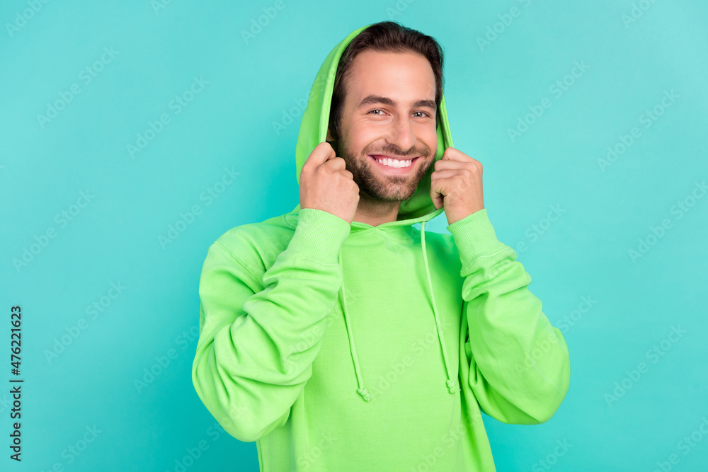 Photo of cheerful confident virile guy toothy smile hold hood wear green hoodie isolated teal color background Photo of cheerful confident virile guy toothy smile hold hood wear green hoodie isolated teal color background