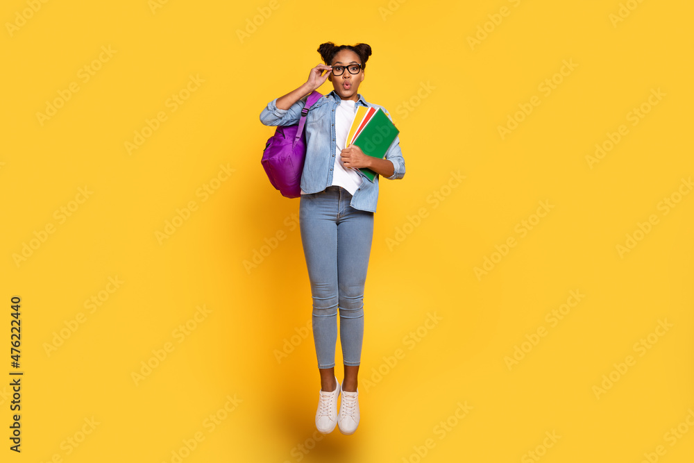 Full body photo of young african girl jump eyewear hold homework lesson isolated over yellow color background