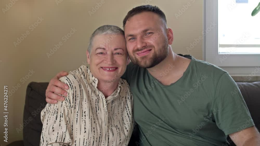 An adult son hugs his mother. An elderly woman has regrowth of hair after chemotherapy. Love, care and support in the family of a cancer patient. An adult son hugs his mother. An elderly woman has regrowth of hair after chemotherapy. Love, care and support in the family of a cancer patient.