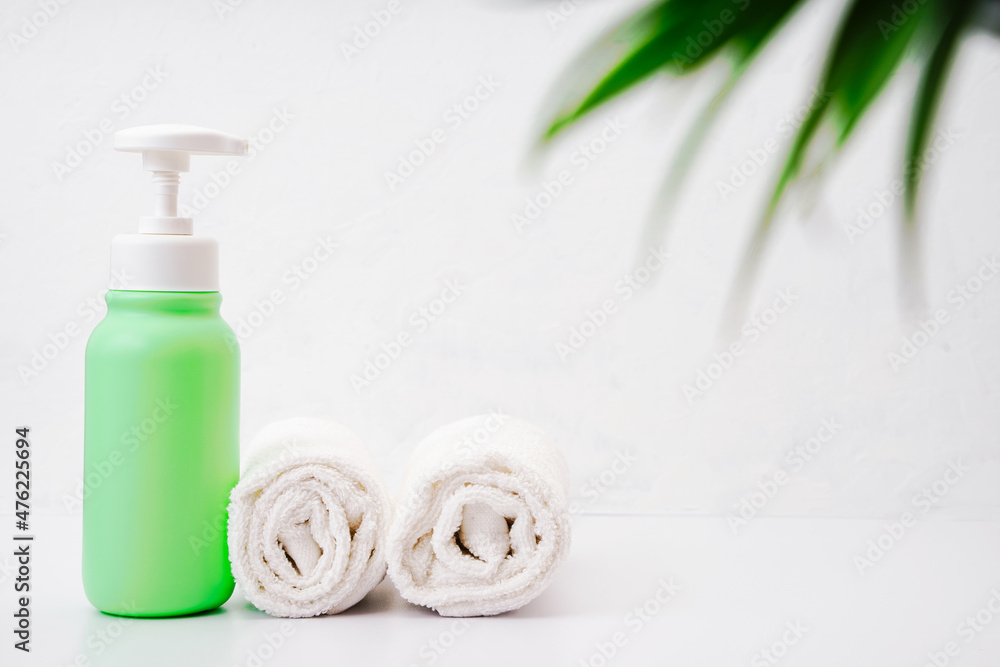 Green bottle of moisturizing lotion and two white cleanliness towels in the bathroom. Body and skin care concept. Copy space Green bottle of moisturizing lotion and two white cleanliness towels in the bathroom. Body and skin care concept. Copy space