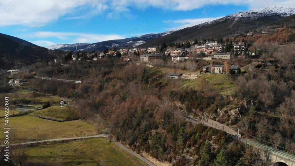 Aerial: passenger train going through a valley in a mountainous landscape and snow covered peaks in the background Aerial: passenger train going through a valley in a mountainous landscape and snow covered peaks in the background