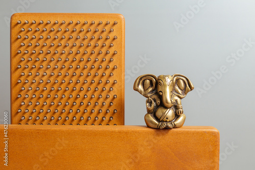 Bronze statue of Lord Ganesha, hindu God.. Brown Sadhu wooden boards with nails for yoga and spiritual practices on the grey background. Meditation, standing on nails, therapy.