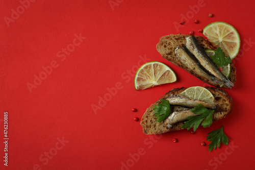 Tasty sandwiches with sprats on red background