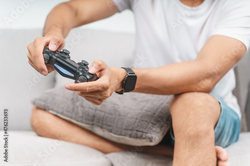 Excited young handsome man holding joystick controller playing video game sitting on the couch at home