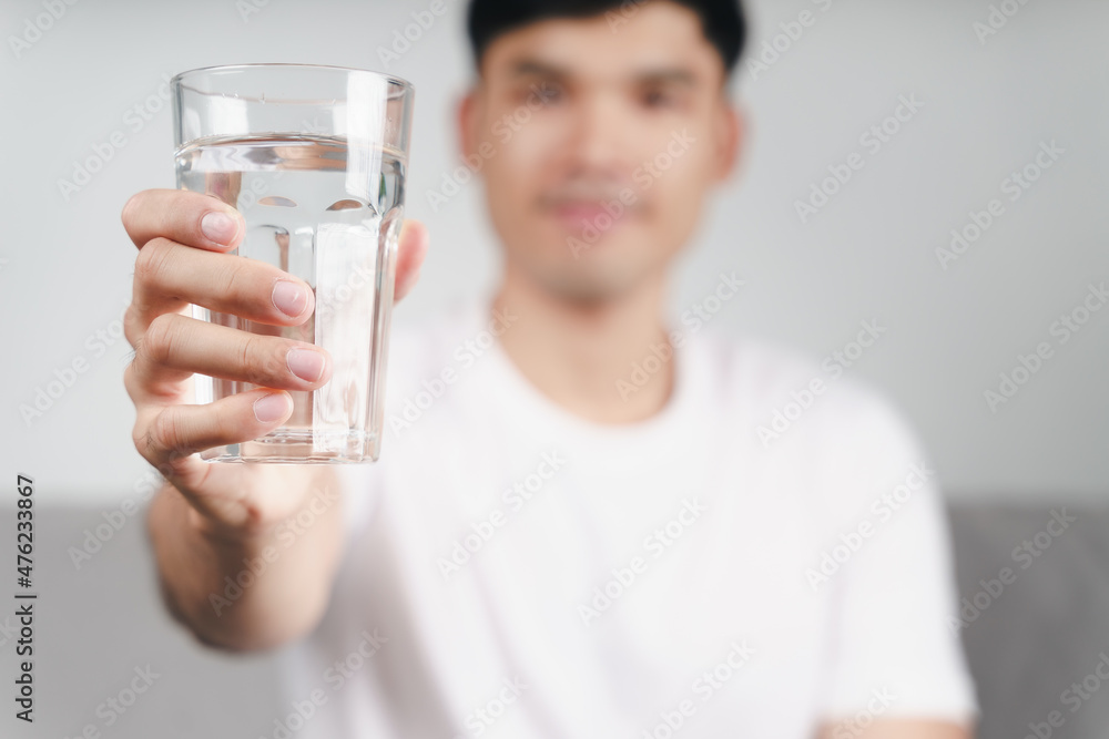 handsome asian man drinking a glass of water on the sofa at living room . handsome asian man drinking a glass of water on the sofa at living room .
