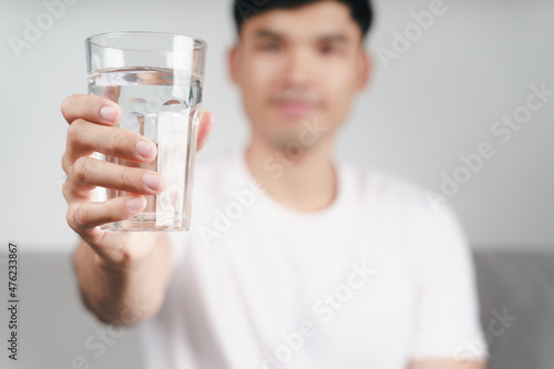 handsome asian man drinking a glass of water on the sofa at living room .