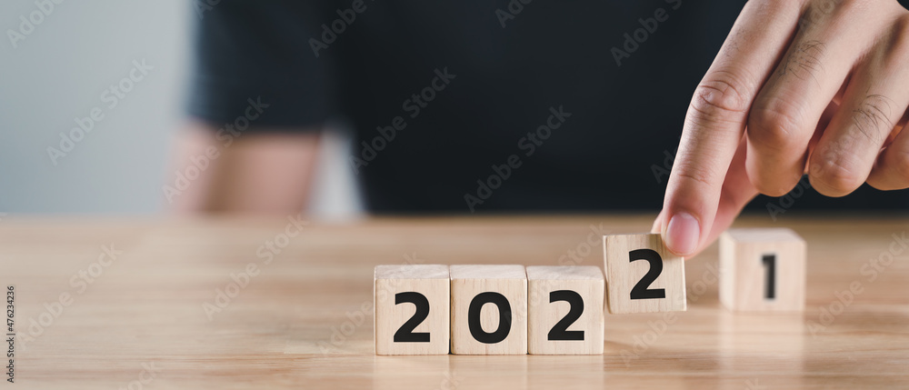 Man hand putting wooden cube block to change 2021 year to 2022 year on wood table with copy space. start to year 2022. happy new years concept. Man hand putting wooden cube block to change 2021 year to 2022 year on wood table with copy space. start to year 2022. happy new years concept.