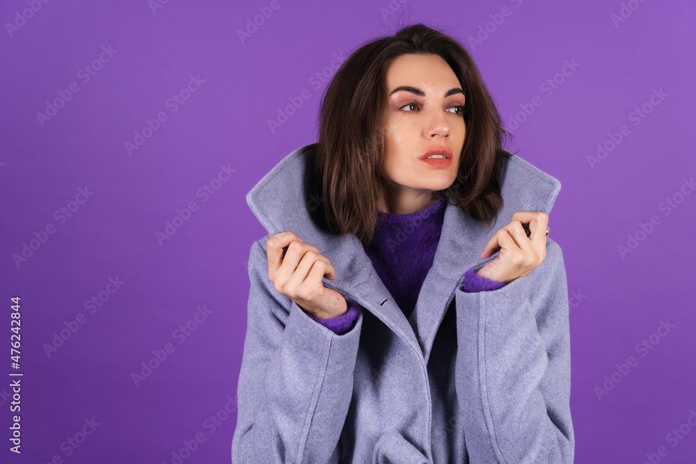 Fototapeta premium Young woman in a gray coat on a purple background posing, cozy and warm, autumn winter style