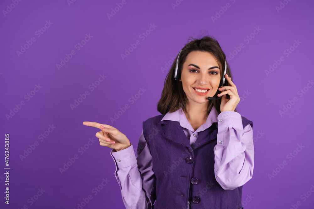 Young woman in a shirt and vest on a purple background manager, call center worker, wearing headphones, a welcome smile, pointing a finger to the left Young woman in a shirt and vest on a purple background manager, call center worker, wearing headphones, a welcome smile, pointing a finger to the left
