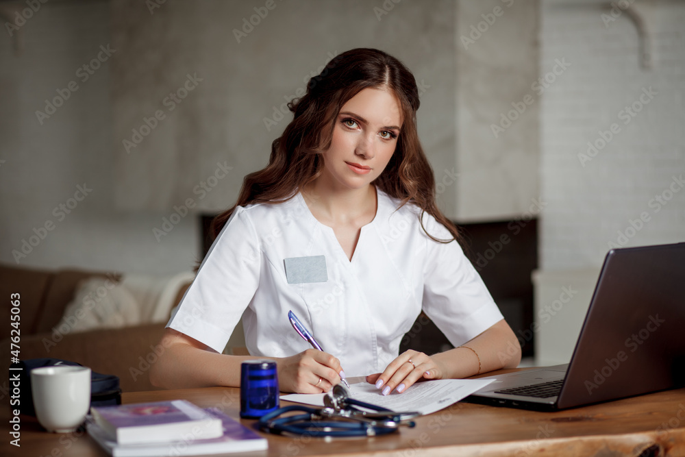 Beautiful nurse in a white medical suit sits at a table in front of a laptop and makes notes. Beautiful nurse in a white medical suit sits at a table in front of a laptop and makes notes.