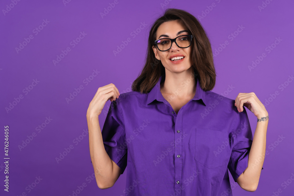 Young woman in a shirt with short sleeves on a purple background, with makeup, lipstick on her lips and stylish glasses smiles broadly