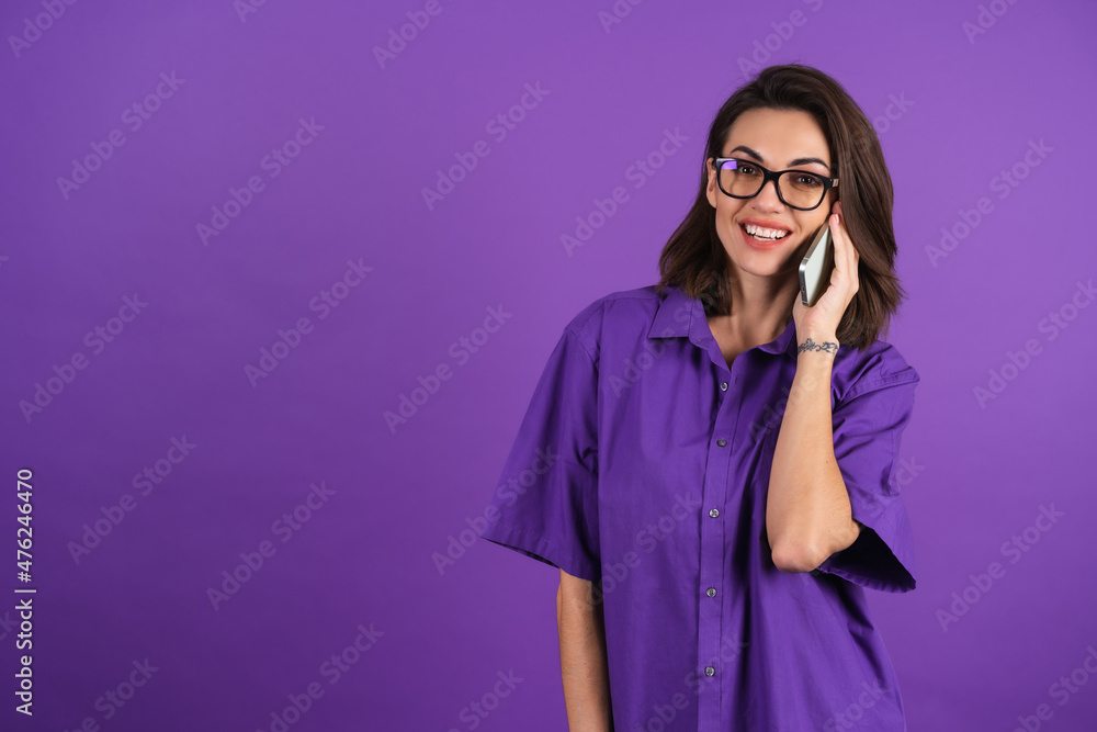 Young woman in a shirt and glasses on a purple background with a phone cheerfully chatting with friends, husband, parents Young woman in a shirt and glasses on a purple background with a phone cheerfully chatting with friends, husband, parents