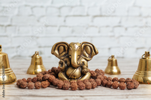 Bronze statue of Lord Ganesha, hindu God. Rudraksha rosary for meditation and set of metal bells for ceremonies on bright wooden background.
