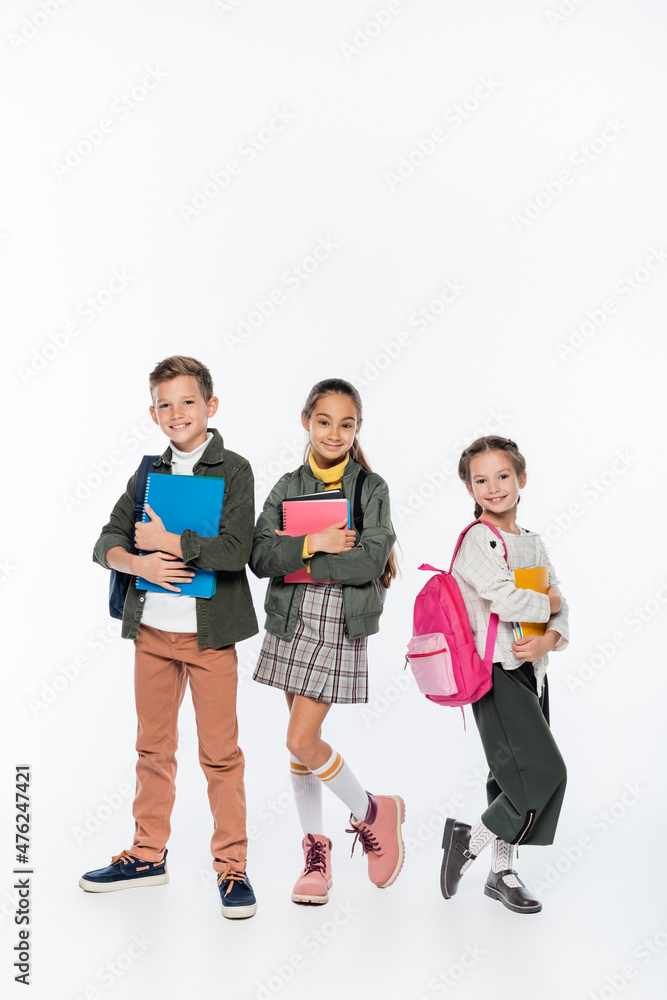 full length of positive schoolboy and schoolgirls standing with backpacks and notebooks on white. full length of positive schoolboy and schoolgirls standing with backpacks and notebooks on white.