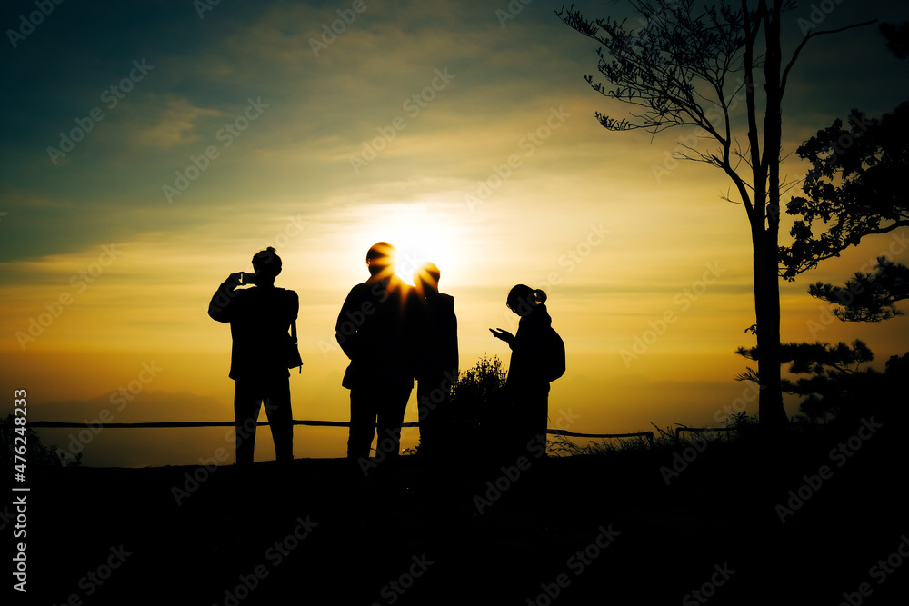 silhouette of a group of teenagers standing and watching the sunrise in the morning On the top of a mountain where the golden yellow sunlight shines , Phu Kradueng National Park ,Thailand