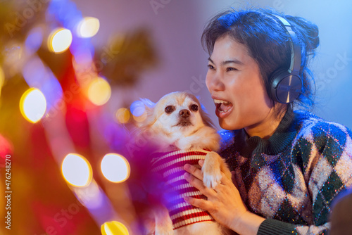 happiness lifestyle with animal dog,friendly smiling asian female woman hold little puppy lap dog while listening music headphone wnjoy christmas new year weelend vacation at night celebrating herself