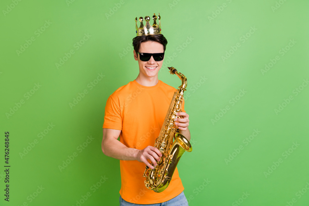 Naklejka premium Photo of cheerful young happy man wear crown good mood hold saxophone isolated on green color background