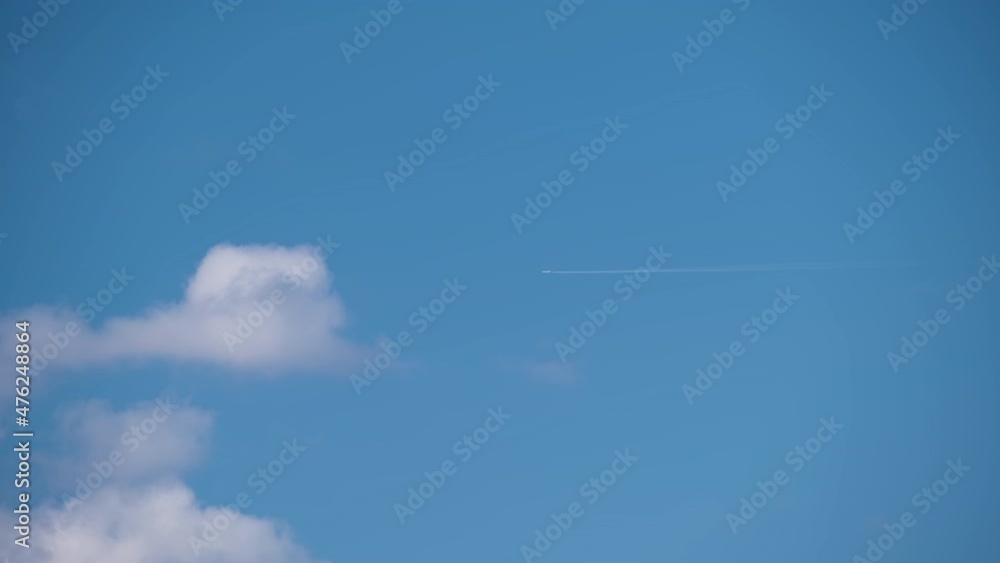 Distant passenger jet plane flying on high altitude on blue sky with white clouds leaving smoke trace of contrail behind. Air traveling concept Distant passenger jet plane flying on high altitude on blue sky with white clouds leaving smoke trace of contrail behind. Air traveling concept