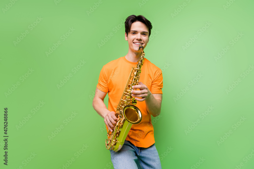 Fototapeta premium Photo of cheerful happy young joyful man hold hands saxophone smile music isolated on green color background
