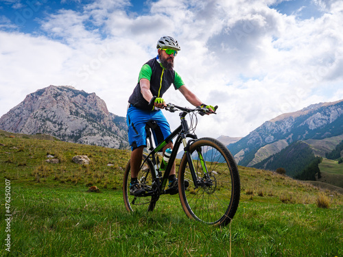 The cyclist rides in the mountains on a summer day. Bearded sportsman on a mountain bike. Outdoor activities