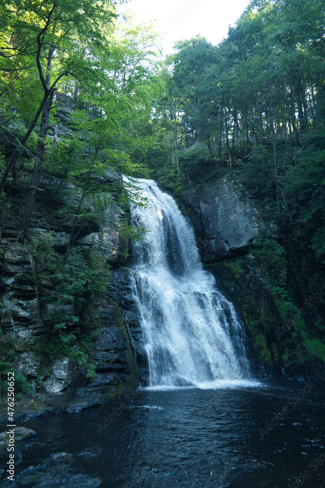 Fototapeta premium Large waterfall pouring out into a beautiful pool of water in the middle of the forest