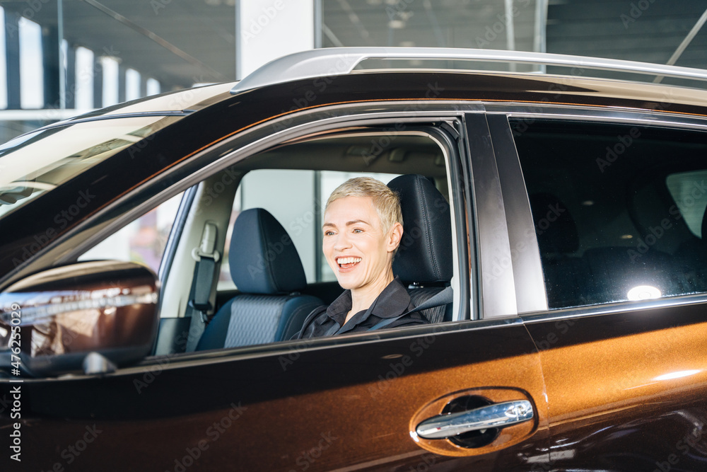 Business woman buying the car. Blond slim caucasian lady in a car salon. Elegant middle age female with short hair in car salon. Business woman buying the car. Blond slim caucasian lady in a car salon. Elegant middle age female with short hair in car salon.