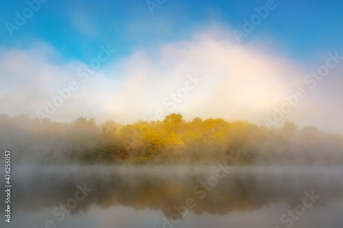 Autumn fog over the river and forest with yellow leaves.