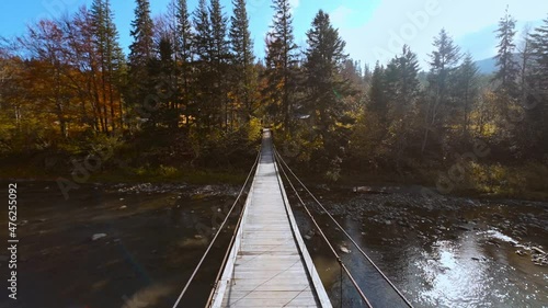 cinematic aerial slow motion b-roll shot of wooden Suspension Bridge hanged over mountain river. amazing landscape with spruces, mountains and sky on background. photo