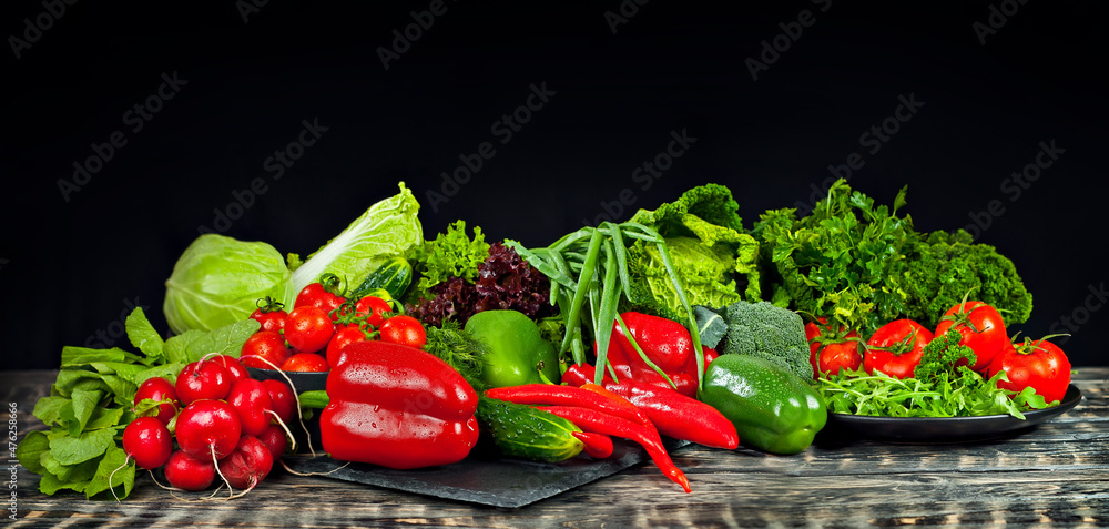 Cabbage, peppers, tomatoes, cucumbers, lettuce, cherry tomatoes, broccoli, arugula on a black background. variety of vegetables on a pile on a wooden table. Cabbage, peppers, tomatoes, cucumbers, lettuce, cherry tomatoes, broccoli, arugula on a black background. variety of vegetables on a pile on a wooden table.