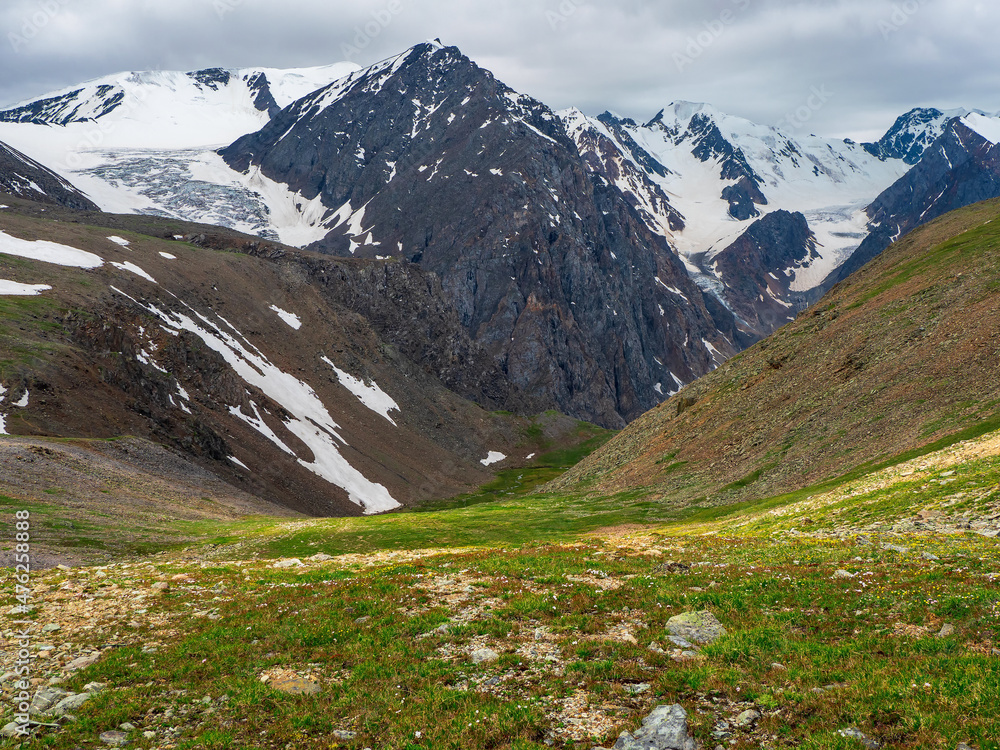 Green mountain slope, a view of a deep mountain valley with stunning snow peaks in the background. Green mountain slope, a view of a deep mountain valley with stunning snow peaks in the background.