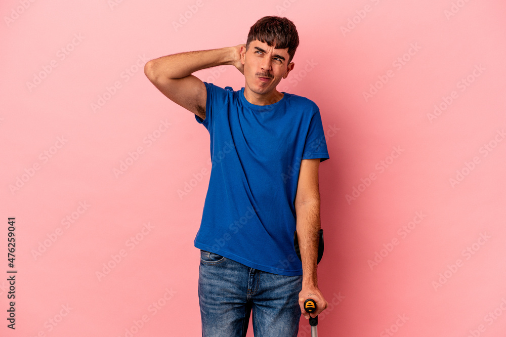 Young mixed race man with crutches isolated on pink background touching back of head, thinking and making a choice. Young mixed race man with crutches isolated on pink background touching back of head, thinking and making a choice.