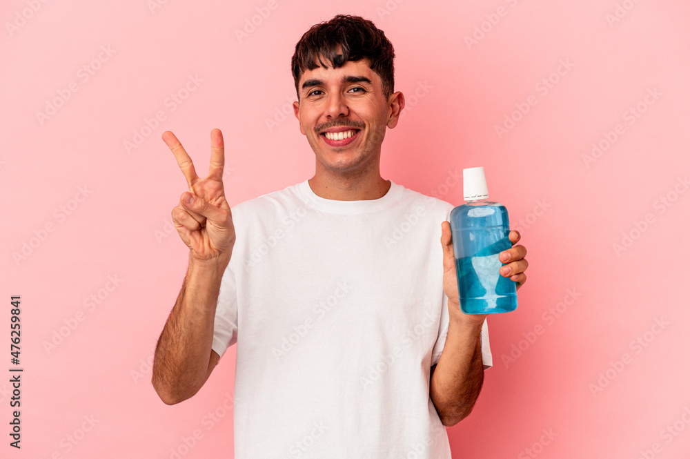Young mixed race man holding mouthwash isolated on pink background showing number two with fingers. Young mixed race man holding mouthwash isolated on pink background showing number two with fingers.