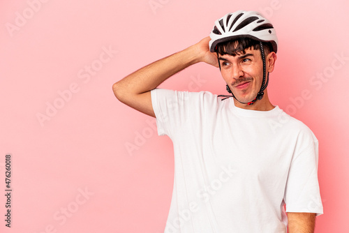 Young mixed race man wearing a helmet bike isolated on pink background touching back of head, thinking and making a choice.